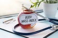 Red apple with text BMI Body Mass Index and measuring tape on background of vegetables and fruits, diet and healthy weight concept