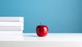Red apple on a white table next to a stack of books against a blue background. Royalty Free Stock Photo