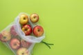 Red apples in eco reusable bag on a green background top view. Eco living concept