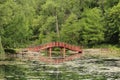 A red arched bridge over a lake leading to walking trails through a forest and around the lake in Janesville, Wisconsin