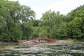 A red arched bridge over a lake leading to walking trails through a forest in Janesville, Wisconsin