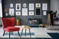 Red armchair next to table on carpet in dark grey living room interior with gallery in blurred background. Real photo Royalty Free Stock Photo