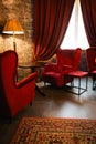 Red armchairs and table with lamp in cozy classic interior. Antique living room with red curtains and armchairs