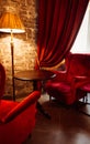 Red armchairs and table with lamp in cozy classic interior. Antique living room with red curtains and armchairs