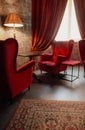 Red armchairs and table with lamp in cozy classic interior, defocused. Antique living room with red curtains and armchairs