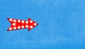 Red arrow shaped vintage colorful illuminated metallic display sign with glowing light bulbs on left side of empty blue wall Royalty Free Stock Photo