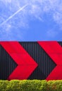 Red arrows pattern on black corrugated metal wall with green bush fence at public health park against jet plane flying on blue sky Royalty Free Stock Photo