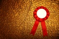 Red award rosette with ribbons over luxury gold brass textured background, ready for mock up