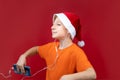 On a red background, a child with a Christmas hat and a yellow T-shirt holds a phone in his hand and listens to music through Royalty Free Stock Photo