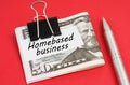 On a red background lies a pen and dollars clamped with a clip with the inscription on paper - Homebased business