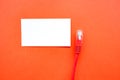 On a red background of paper is an empty business card and an Internet cable with a connector Royalty Free Stock Photo