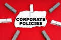 On a red background, there are clothespins and a piece of paper with the inscription - Corporate Policies