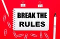 On a red background, a white pen, white paper clips, a white pencil and a notebook with the text BREAK THE RULES. View from above Royalty Free Stock Photo