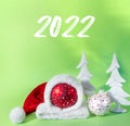 Red ball in  hat of santa claus with white spruce tree on green background. The symbol of new year and christmas Royalty Free Stock Photo