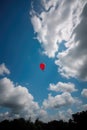 Red balloon in cloudy blue sky over tree tops, copy space, created using generative ai technology Royalty Free Stock Photo