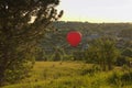 Red balloon flies over a village located between picturesque hills. Clear blue sky without clouds, during sunset Royalty Free Stock Photo