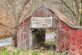 Red barn with faded paint and old sign covered in vines during late winter