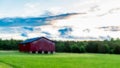 Red barn in a field with sky and clouds in the background Royalty Free Stock Photo