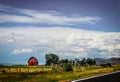 Red barn and outbuildings on farm along blacktopped highway with mountains in distance and pretty sky with fluffy clouds