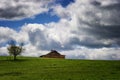 Red Barn sits on a green hillside under cloudy skies