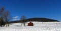 Red barn sits on hillside with white snow and blue sky Royalty Free Stock Photo