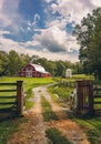 Red barn and white horse trailer on farm with dirt road and wooden fence in the foreground and trees in the background Royalty Free Stock Photo