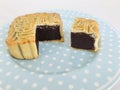 Red Bean Paste moon cake with a portion cutout in a blue spotted round dish on marble background.