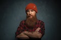 Red bearded man with orange hat and plaid shirt on dark cyan background