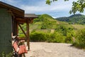 A red bench standing on the hill of the winery next to a wooden house, in the background beautiful vineyards in the spring.