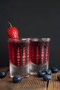 Red berries liqueur in shot glass isolated on black background and wooden table. Homemade alcohol drink concept.