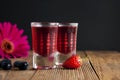 Red berries liqueur in shot glass isolated on black background and wooden table. Homemade alcohol drink concept.