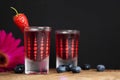 Red berries liqueur in shot glass isolated on black background and wooden table. Homemade alcohol drink concept. Royalty Free Stock Photo
