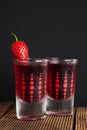 Red berries liqueur in shot glass isolated on black background and wooden table. Homemade alcohol drink concept.