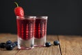 Red berries liqueur in shot glass isolated on black background and wooden table. Homemade alcohol drink concept. Royalty Free Stock Photo