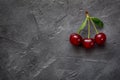 Red berries of ripe cherries with green leaves on a black craft background. Close-up photo of a berry.