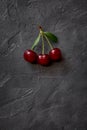 Red berries of ripe cherries with green leaves on a black craft background. Close-up photo of a berry.