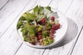 Red berries of wild raspberries in a white plate on a wooden table, a branch of raspberries with green leaves, organic Royalty Free Stock Photo