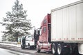 Red big rig broken semi truck with open hood and repair road assistant vehicle standing on the snowy winter road side shoulder Royalty Free Stock Photo