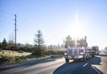 Red big rig day cab semi truck transporting commercial cargo on flat bed semi trailer running in front of semi trucks convoy on Royalty Free Stock Photo