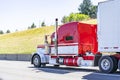 Red big rig long cab classic semi truck transporting frozen cargo in reefer semi trailer driving on the road in sunny day Royalty Free Stock Photo