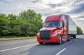 Red big rig long haul semi truck with black grille transporting cargo in dry van semi trailer running on the wide highway road Royalty Free Stock Photo