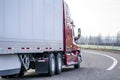 Red big rig long haul semi truck transporting dry van semi trailer turning on the local road