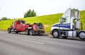 Red big rig semi towing truck prepare to tow broken white big rig semi tractor standing out of service on the road side Royalty Free Stock Photo