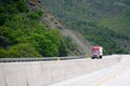 Red big rig semi truck with semi trailer going up hill on winding green highway in mountain Royalty Free Stock Photo