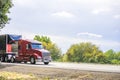 Red big rig semi truck transporting covered semi truck with front wall spoiler running on the road