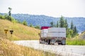 Red big rig semi truck transporting lumber wood on two semi trailers driving on winding road with hills