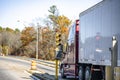 Red big rig shiny semi truck with dry van semi trailer standing on the highway entrance with traffic light Royalty Free Stock Photo