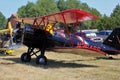 A Red and Black Airplane at a Flying Farmers show sitting by the runway by the airplane hanger on a colorful day.