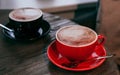 Red and black ceramic cups of cappuccino on wooden table inn a cafe. Mockup for your design. Royalty Free Stock Photo