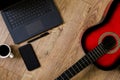 Red-black classical guitar standing on wooden floor, next to computer, phone, coffee and notebook-pen Royalty Free Stock Photo